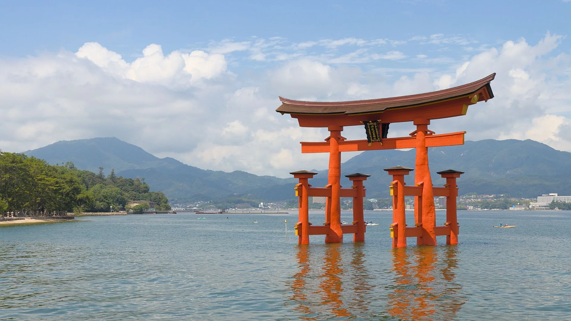 Den cinnoberrøde torii-port ved Itsukushima Shrine, der står i havet ud for Miyajima, med bjergene ved Seto Inland Sea bag sig