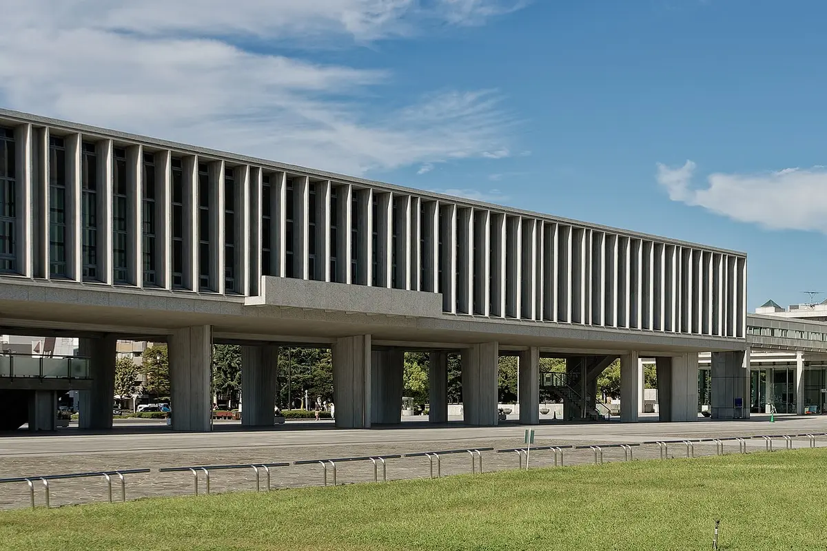 The long concrete Main Building of the Hiroshima Peace Memorial Museum raised on columns, under a blue sky