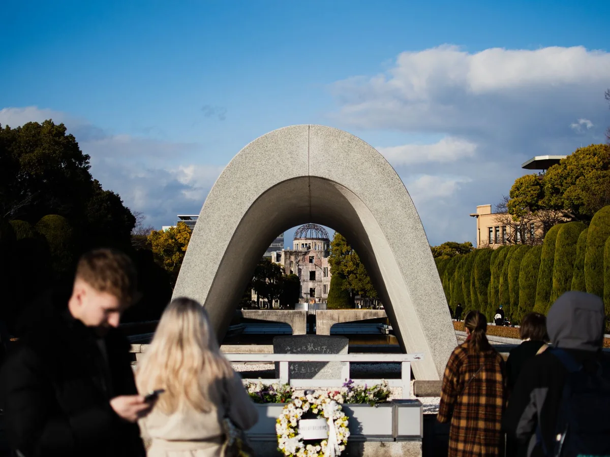 Visitatori al Cenotafio del Memoriale nel Parco del Memoriale della Pace di Hiroshima, con la Cupola della Bomba Atomica visibile attraverso l'arco